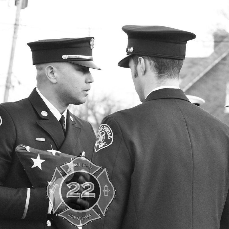 Hector Martinez in Pontiac FD dress uniform holding a folded American flag at a department ceremony