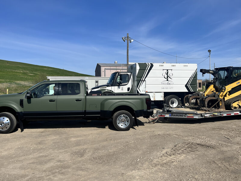 Trees and Co. branded chip truck with skid steer at a job site
