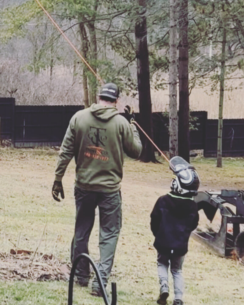 A Trees and Co. crew member in a branded hoodie walking to a worksite with his son